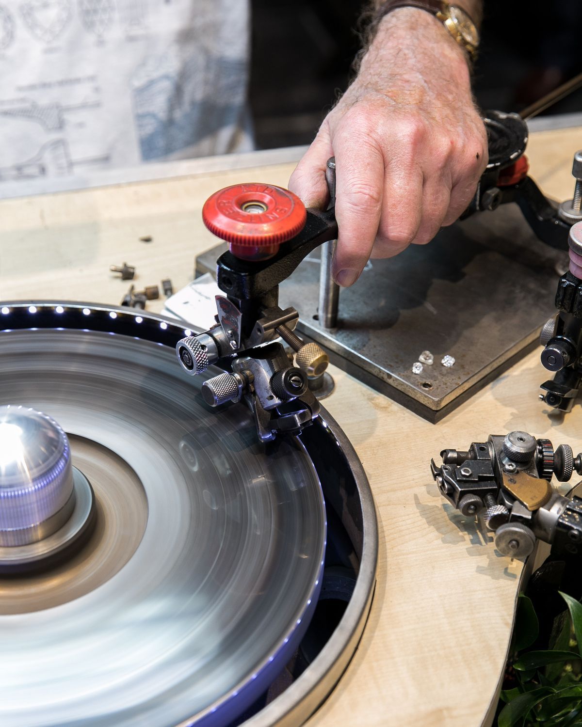 A diamond cutter's hand guiding a stone on a spinning polishing wheel