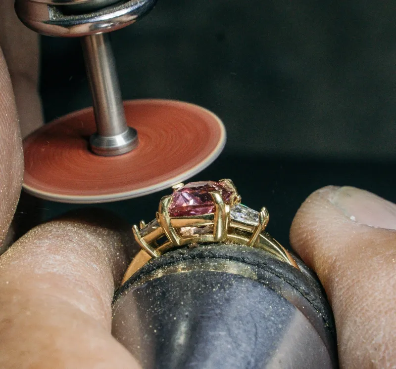 A jeweler polishing a pink sapphire and diamond ring in yellow gold